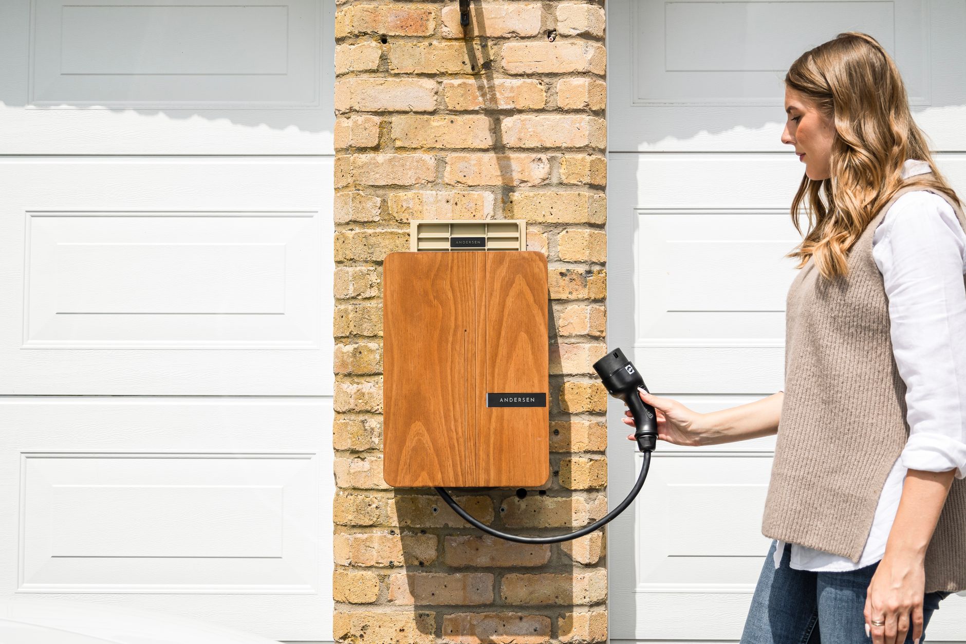 Laadpaal aan de garagemuur met laadkabel in de hand